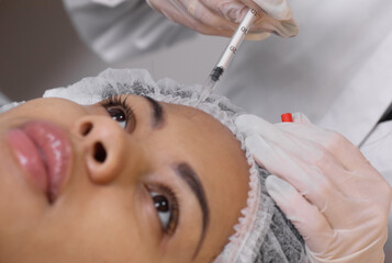 Cosmetologist makes rejuvenating anti wrinkle injections on the face of a beautiful black woman....