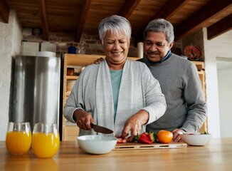 Multi-cultural elderly couple laughing in modern kitchen. Healthy retired lifestyle at home, preparing fruit salad.