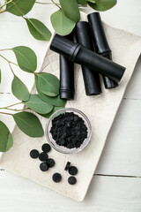 Bowl with activated charcoal tooth powder, pills and bamboo sticks on white wooden background