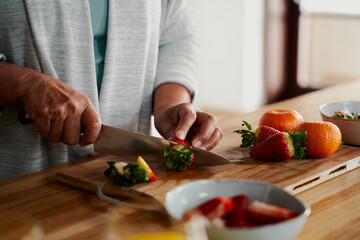 Hands of biracial elderly female chopping strawberries in modern kitchen. Preparing healthy meal...
