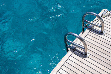 Boat back deck, teak wood and metal ladders, blue sea water background. Luxury yacht cruise