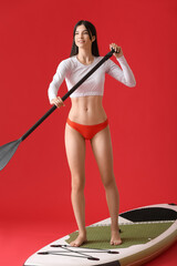 Sporty young woman with board for sup surfing and oar on color background