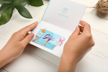 Female hands with gift card on white wooden table