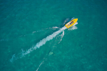 Boat performance fast movement on clear water aerial view. Yellow high-speed luxury boat with people moving on turquoise water.