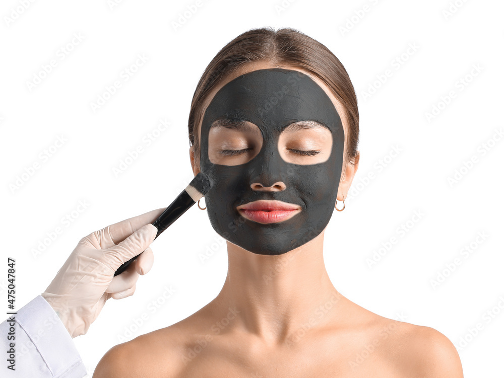 Canvas Prints Cosmetologist applying activated charcoal mask on woman's face against white background