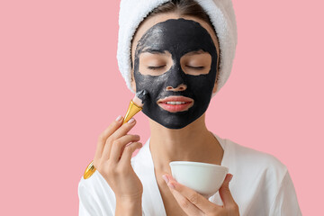 Young woman applying activated charcoal mask on her face against color background