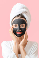 Young woman with activated charcoal mask on her face against color background