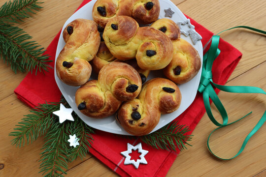 Traditional swedish saffron buns with raisins called Lussekatter on a plate on wooden table with festive Christmas decorations. Homemade baked buns