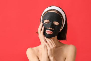 Young woman with activated charcoal mask on her face against color background