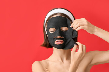 Young woman with activated charcoal mask on her face against color background