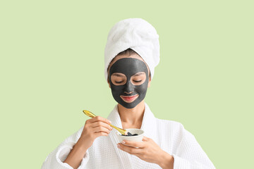 Young woman with activated charcoal mask on her face against color background