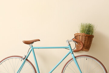 Modern bicycle with wicker basket and green grass near beige wall