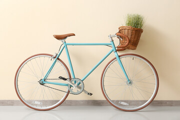 Fototapeta na wymiar Modern bicycle with wicker basket and green grass near beige wall