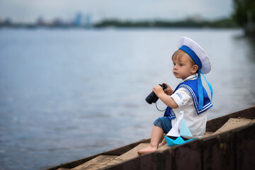 Handsome little boy stands on the shore with binoculars, looks at ships and yachts and plays with a boat