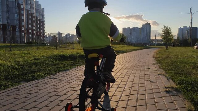Happy boy riding bike, having fun outdoors on nature. A child rides a bicycle in the city on a sunset background. Active sport family leisure. Back view.