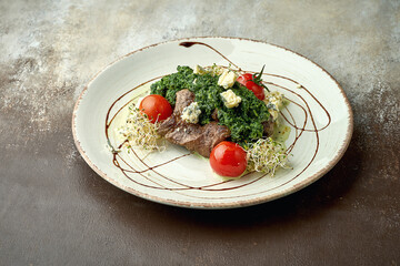 Beef steak with stewed creamy spinach in a plate on a brown background