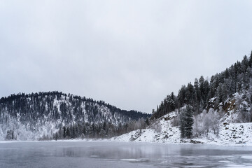 Winter mountain landscape. River near snowy mountains overgrown with fir trees