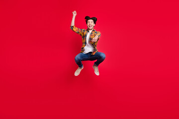 Photo of funky sweet young guy dressed checkered clothes jumping high riding horse smiling isolated red color background