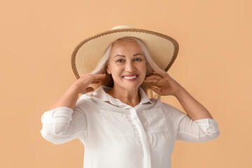 Beautiful mature woman in stylish hat adjusting her hair on color background