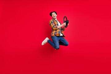 Fototapeta na wymiar Photo of cute funky guy dressed checkered clothes jumping high holding steering wheel smiling isolated red color background