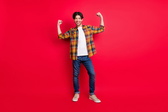 Photo of pretty strong young guy dressed checkered clothes showing arm muscles smiling isolated red color background