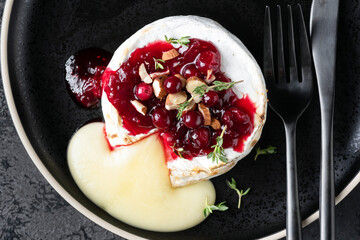 Baked camembert cheese with cranberries and nuts served on black plate, top view