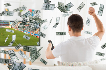 online betting, gambling and sport concept - happy man watching soccer game on tv with raised fist over money rain
