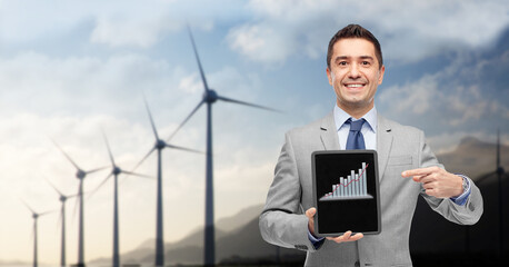 business, technology and green energy concept - smiling businessman with charts on tablet pc computer screen over wind turbines on background