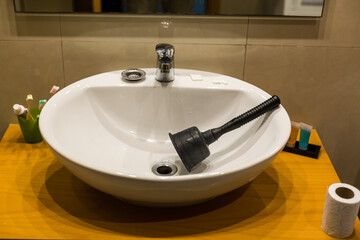 Close-up of plumbers using plunger in bathroom sink.