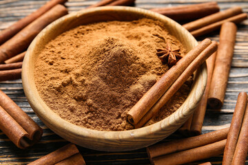 Bowl of natural cinnamon powder and sticks on wooden background, closeup