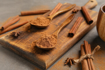 Wooden board with cinnamon powder and sticks on dark background