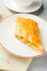 Plate with piece of tasty apple strudel on light background