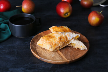 Plate with tasty apple strudel and cup of coffee on black background