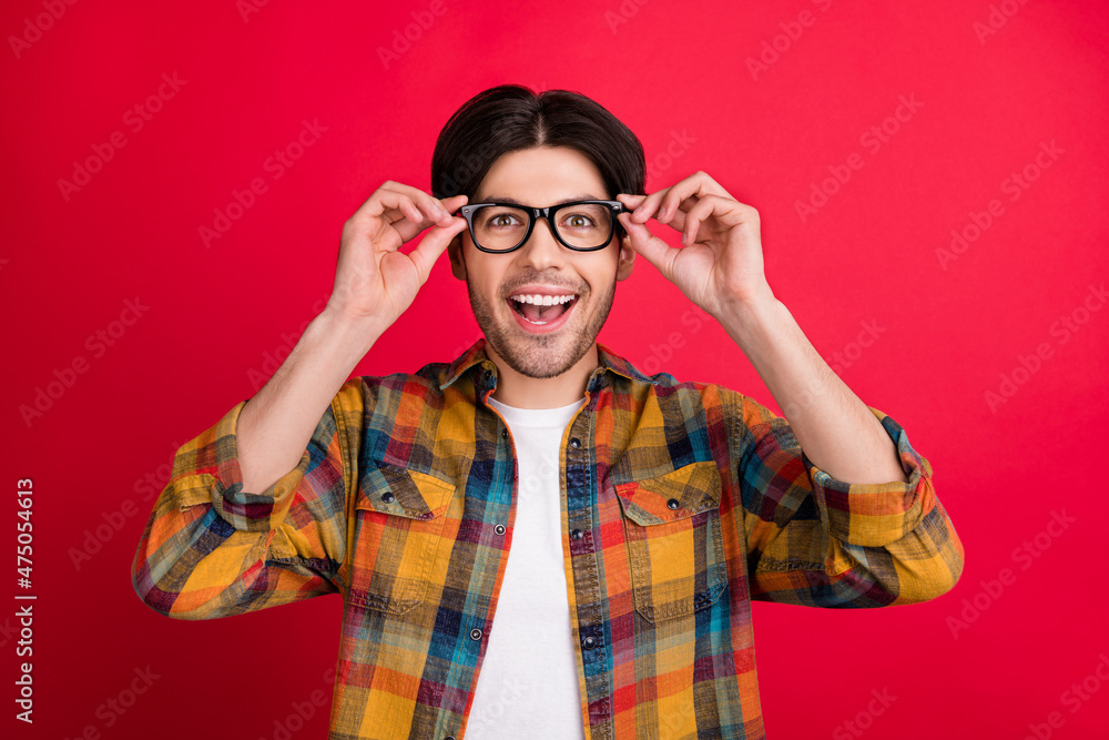 Poster Photo of clever impressed young guy dressed checkered clothes arms glasses smiling isolated red color background