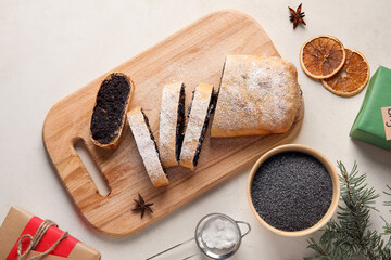 Wooden board with cut poppy seed strudel on light background