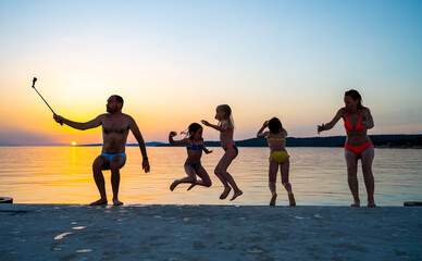 Fototapeta premium Family jumping from pier in the water at sunset.