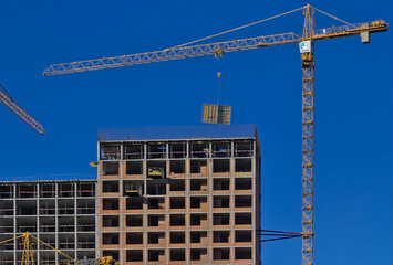 Fototapeta premium Kyiv, Ukraine - On the top floor of the new building under construction, large-sized structures are installed using a crane. Construction of a modern residential complex. Blue sky.
