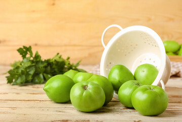 Overturned colander with green tomatoes on wooden background