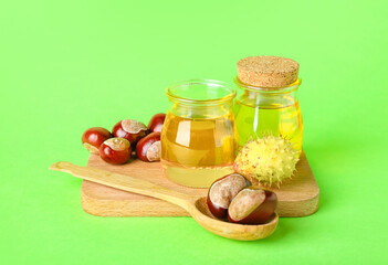 Wooden board with bottles of essential oil and fresh chestnuts on green background