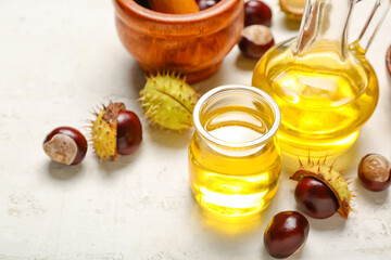Bottle of essential oil and chestnuts on light background, closeup