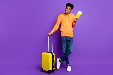 Full body photo of charming brunette afro american young man hold tickets wear jeans luggage isolated on violet color background