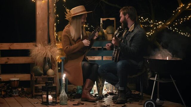 Man and a woman play musical instruments by the campfire