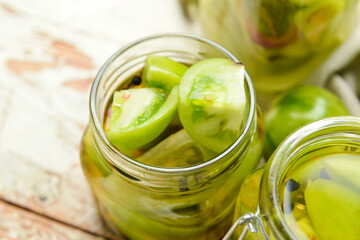 Jars with canned green tomatoes on white wooden background, closeup