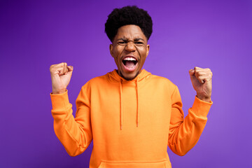 Photo of cheerful young dark skin man winner good mood celebrate champion fists isolated on purple color background