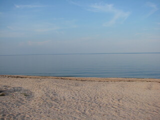 Panorama of the sandy beach near the crystal clear waters of the calm sea on a background of barely cloudy evening sky.