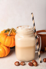 Mason jar of tasty pumpkin latte on light background