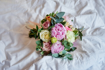 wedding bouquet with peonies lies on a white sheet
