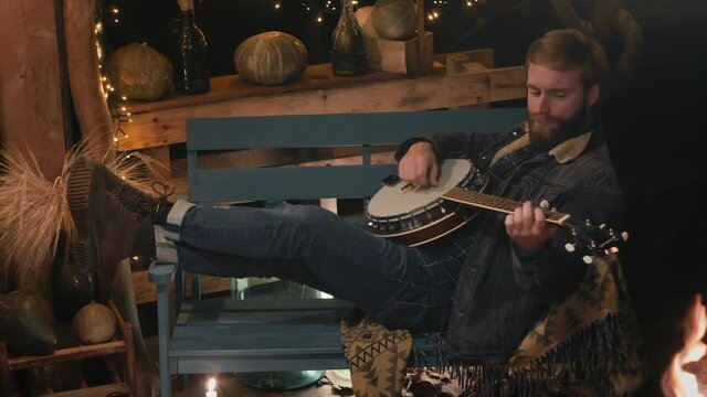 Man in the evening on the veranda plays the banjo lying on a bench