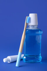 Wooden toothbrush, paste and mouthwash on blue background