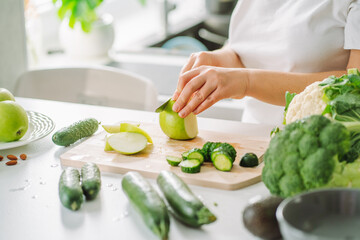 Woman preparing food in her kitchen. Female chopping fresh green apple on cutting board in light kitchen. Healthy eating, detox, diet.